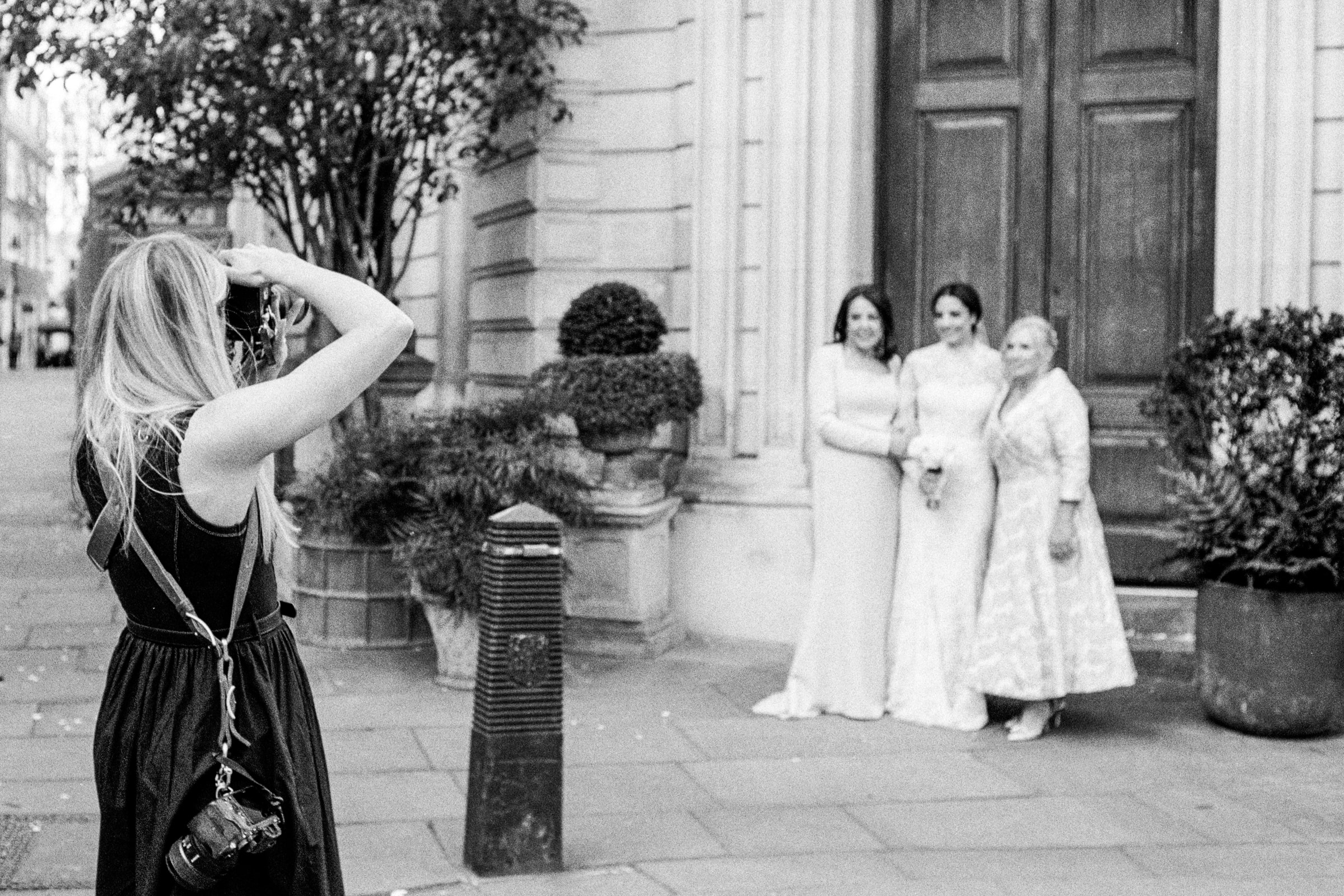 Photographer frames three dressed-up women posing outside a grand doorway in London