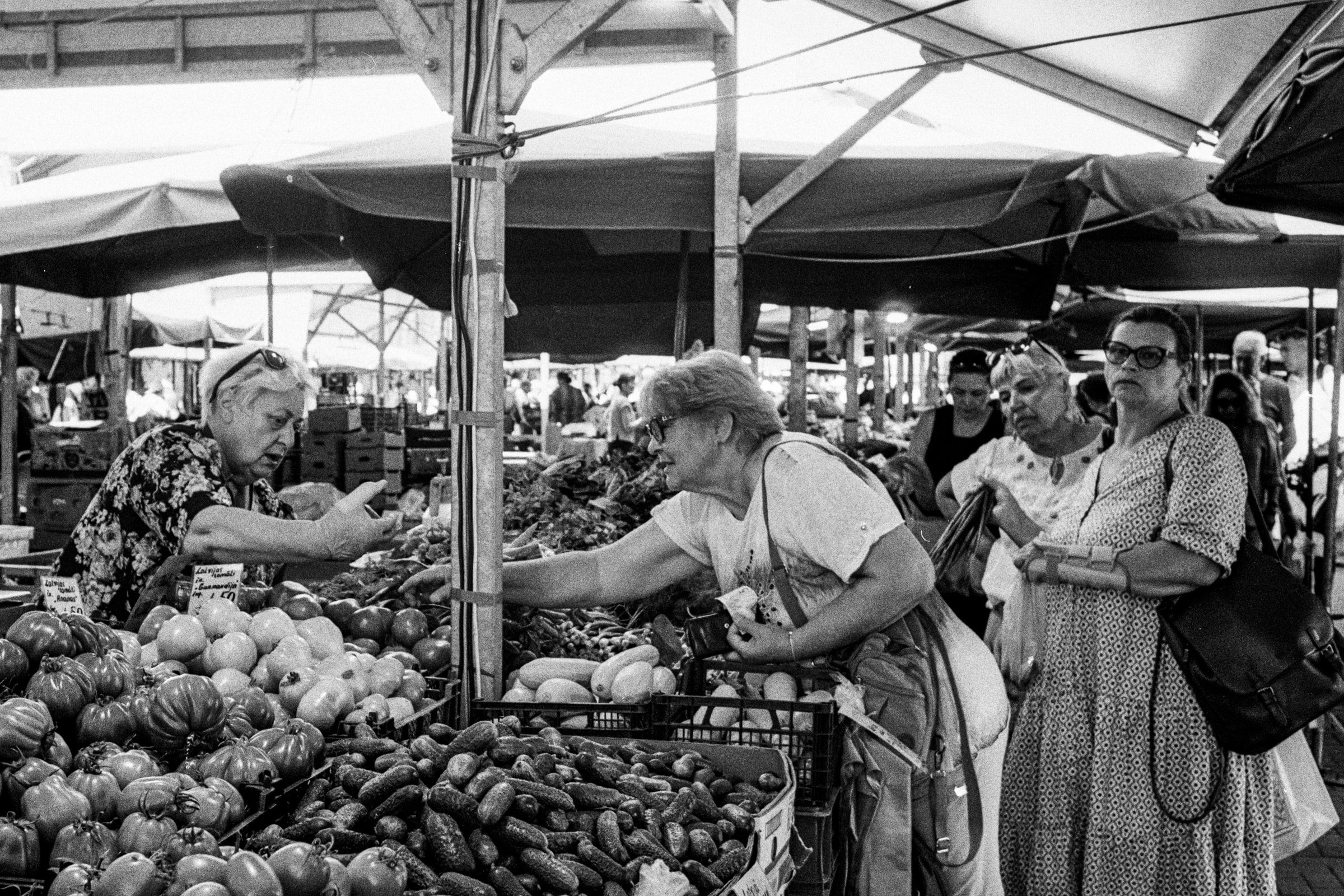 Women shop for vegetables at a crowded covered market stall in Riga.